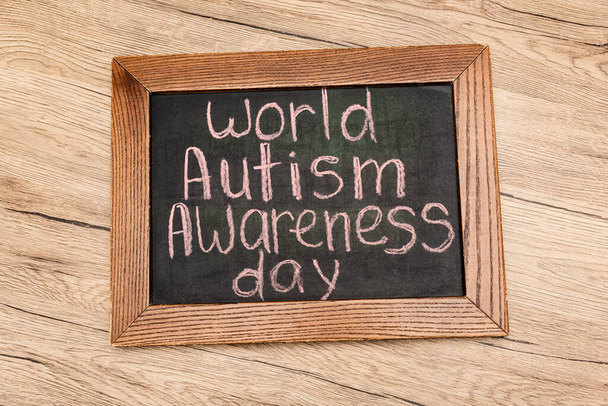 Top view of board with world autism awareness day lettering on wooden background - Фото, изображение