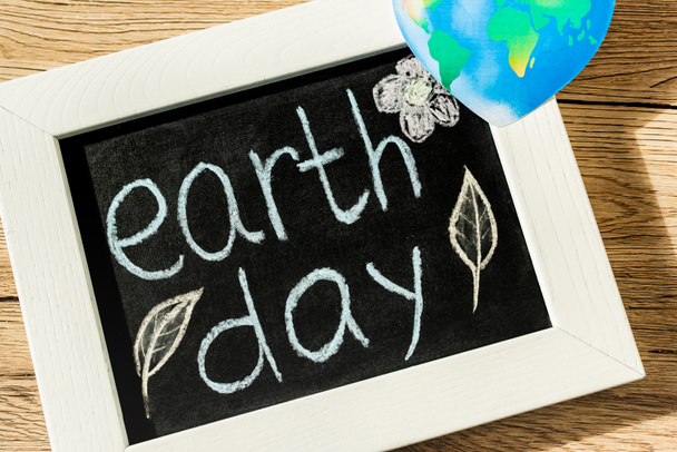 Top view of black board with earth day lettering and globe on wooden background - Фото, зображення