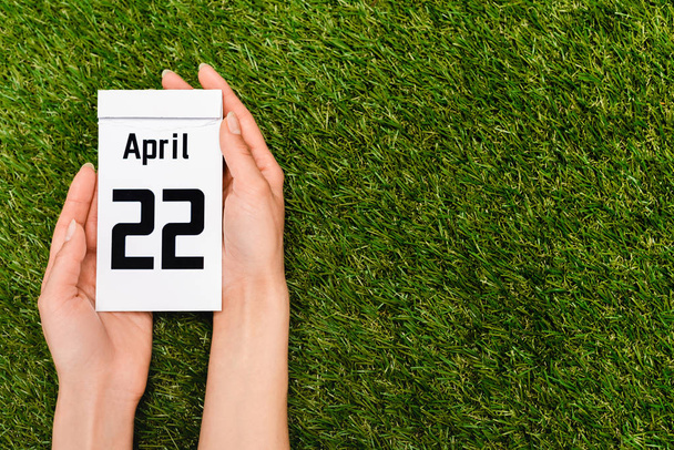 Ausgeschnittene Ansicht des Kalenders mit 22 April-Inschrift in weiblichen Händen auf grünem, Earth Day-Konzept - Foto, Bild