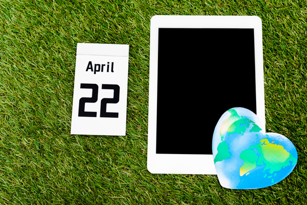 Vista superior de la tableta digital, globo y calendario con 22 inscripción de abril sobre fondo verde, concepto del día de la tierra
 - Foto, Imagen