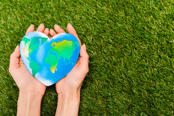 Gewassen beeld van de globe in vrouwelijke handen op groene, dag van de aarde concept - Foto, afbeelding