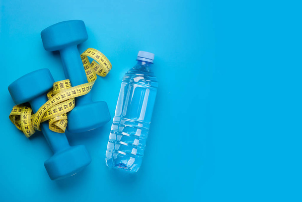 Fitness equipment and water bottle on a blue background. Top view flat lay with copy space - Foto, afbeelding