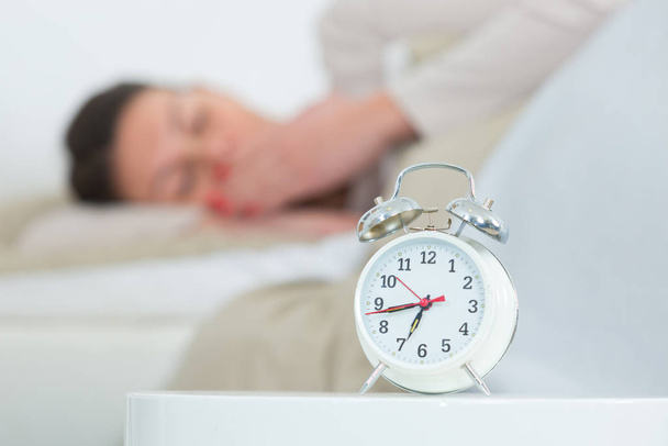 close up of alarm clock and woman sleeping in background - Photo, image