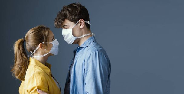 Young romantic loving couple wearing a protective face mask and staring at each other's eyes, pandemic and feelings concept - Foto, afbeelding