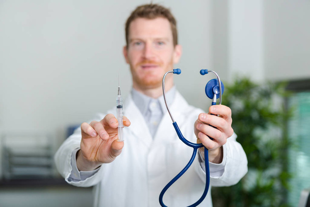 confident young male doctor with stethoscope holding syringe - Фото, зображення