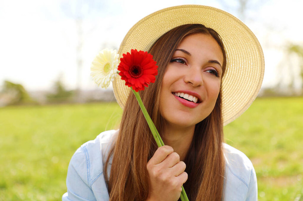 Vidám, romantikus lány két virágot tart a kezében, mosolyog, és a Városliget oldalára néz. - Fotó, kép