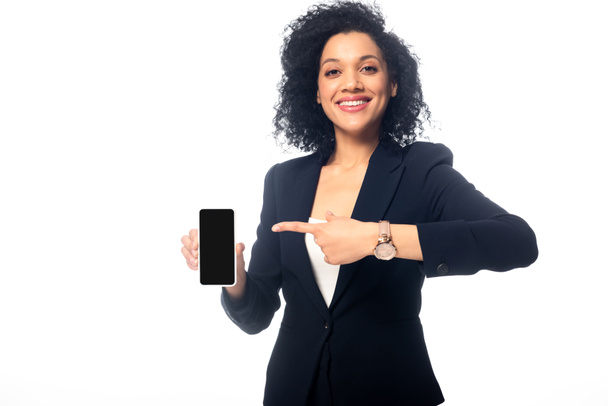 Vista frontal de una mujer afroamericana apuntando al teléfono inteligente, sonriendo y mirando a la cámara aislada en blanco
 - Foto, imagen