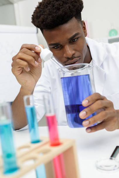 νεαρός επιστήμονας ρίχνει υγρό σε μια φιάλη - Φωτογραφία, εικόνα