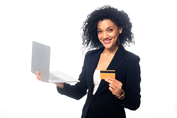 Happy african american businesswoman with laptop showing credit card and looking at camera isolated on white - Foto, Imagen
