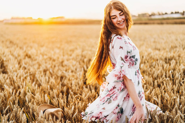Ongelooflijke jonge vrouw met lang krullend haar en sproeten gezicht. Vrouw in jurk poserend in tarweveld bij zonsondergang. Close-up portret. - Foto, afbeelding