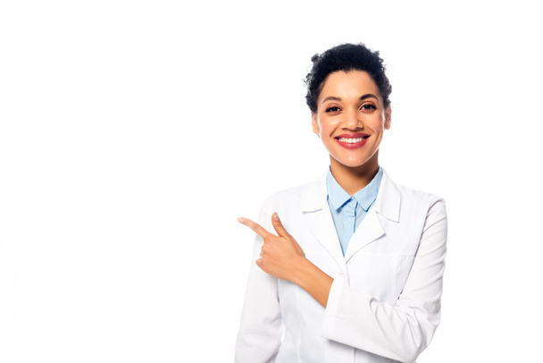 Front view of positive african american doctor looking at camera, smiling and pointing with finger isolated on white - Фото, изображение