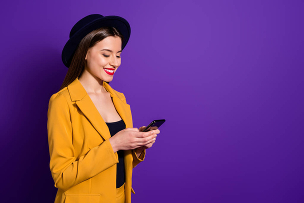 Turned photo of positive cheerful girl blogger use her smartphone read social network news follow posts enjoy wear yellow blazer bright headwear isolated over violet color background - Valokuva, kuva