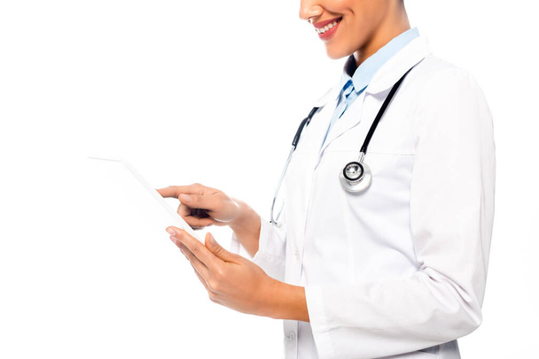 Vue recadrée du médecin afro-américain avec stéthoscope à l'aide d'une tablette numérique et sourire isolé sur blanc
 - Photo, image