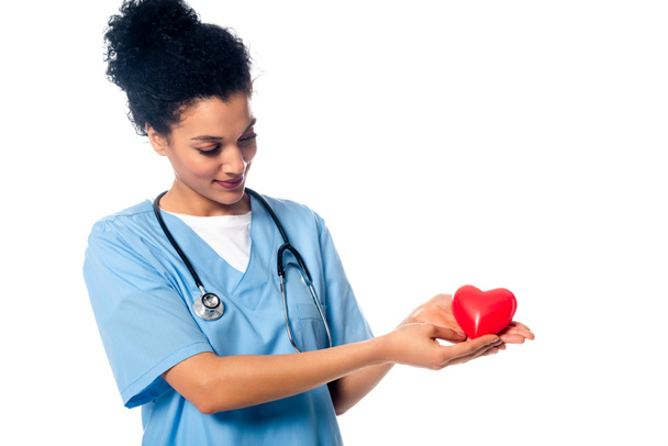 Enfermera afroamericana con estetoscopio mostrando corazón rojo decorativo y sonriendo aislada en blanco
 - Foto, Imagen