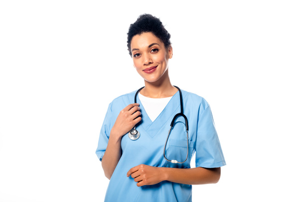 Vorderansicht einer afrikanisch-amerikanischen Krankenschwester mit Stethoskop, die lächelt und isoliert auf weiß in die Kamera blickt - Foto, Bild