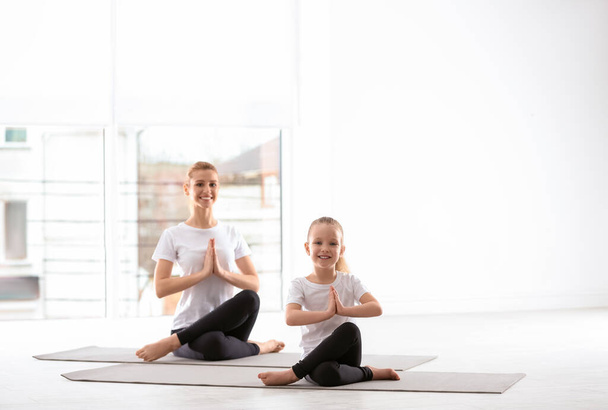 Mother and daughter in matching sportswear doing yoga together at home - Фото, изображение