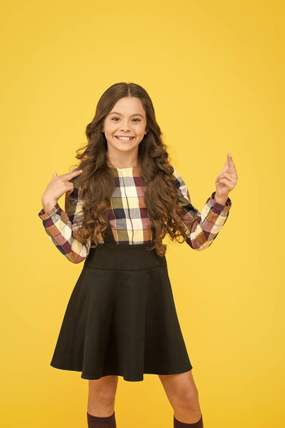 Look up. Happy girl in school fashion pointing finger up. Small child smiling and pointing yellow background. Using pointing gesture to direct attention. Upwards pointing - Photo, Image
