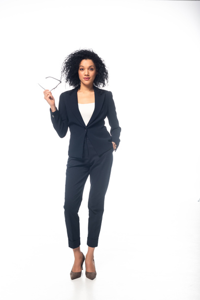 Full length view of confident african american businesswoman in suit with glasses on white  - Fotó, kép