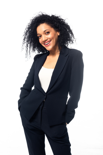 Vista frontale di donna d'affari afroamericana con le mani in tasca sorridente e guardando la fotocamera isolata su bianco
 - Foto, immagini