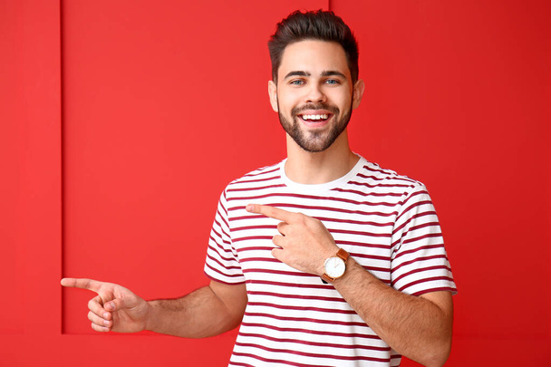 Handsome young man pointing at something on color background - Foto, Bild