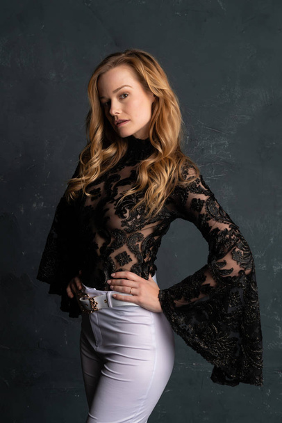 Beautiful tall blonde woman in a black lace blouse and white slacks - Фото, изображение