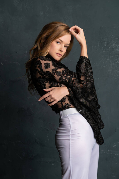 Beautiful tall blonde woman in a black lace blouse and white slacks - 写真・画像