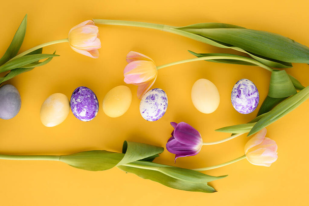 top view Easter yellow background with pink and purple tulips and Easter eggs - Foto, Imagen
