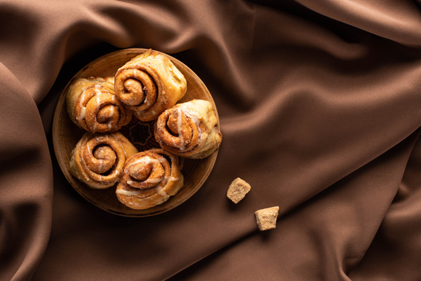 top view of fresh homemade cinnamon rolls on silk brown cloth with brown sugar - Фото, изображение