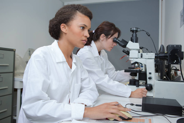 Women working in laboratory using computer and microscope - Фото, зображення