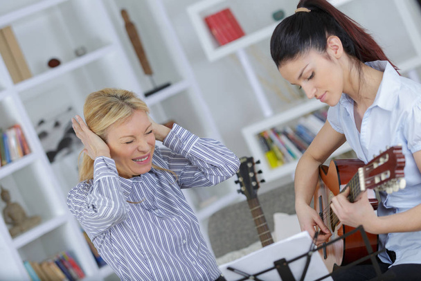 woman annoyed at daughter who is playing a guitar - Фото, зображення