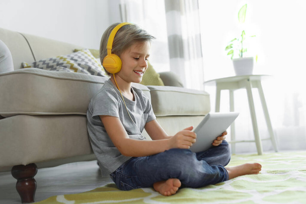 Cute little boy with headphones and tablet listening to audiobook at home - Fotó, kép