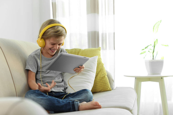 Aranyos kisfiú fülhallgatóval és táblagéppel audiobook hallgatása otthon - Fotó, kép