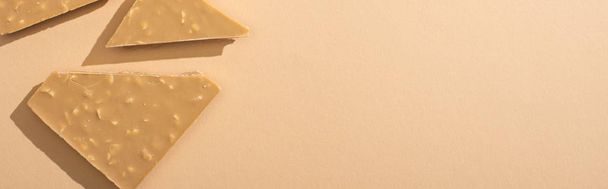 top view of delicious broken white chocolate bar on beige background, panoramic shot - Foto, Imagem