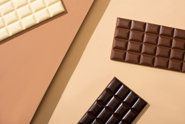 top view of delicious white, milk and dark chocolate bars on beige background - 写真・画像