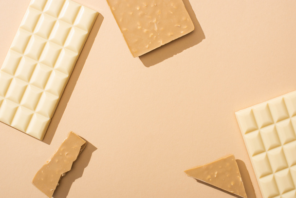 top view of delicious broken and whole white chocolate bars on beige background - Фото, изображение
