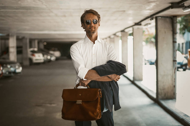 Charming businessman standing at a perking lot holding his jacket and briefcase - Photo, Image