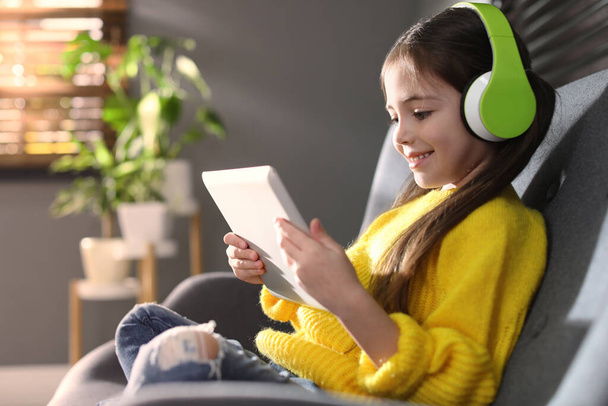 Cute little girl with headphones and tablet listening to audiobook at home - Φωτογραφία, εικόνα