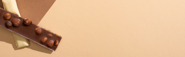 vista superior de delicioso chocolate blanco y leche con nueces sobre papel sobre fondo beige, plano panorámico
 - Foto, Imagen