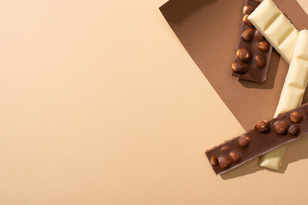 Beyaz ve sütlü çikolatanın bej arka planda fındıklı üst görüntüsü. - Fotoğraf, Görsel