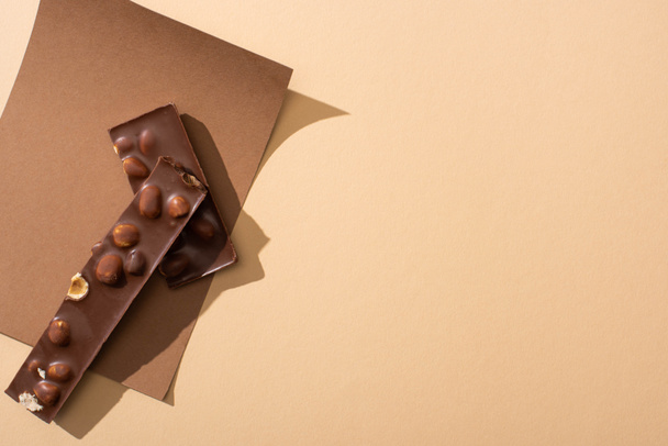 top view of delicious  milk chocolate with nuts pieces on paper on beige background - Photo, Image