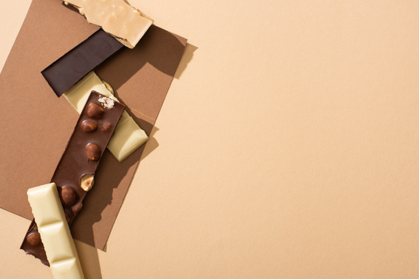 top view of delicious dark, white and milk chocolate with nuts on paper on beige background - Photo, Image