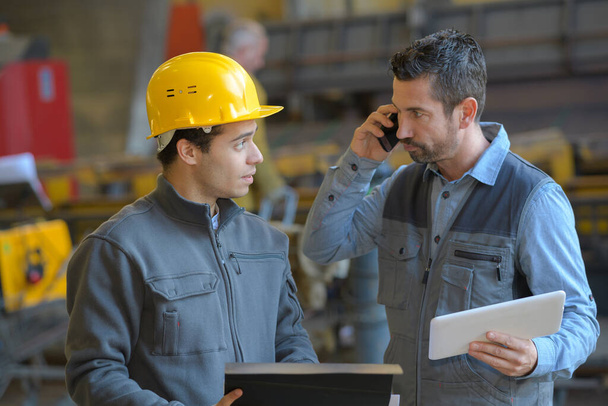 male supervisor talking on mobile phone with worker at industry - Photo, image