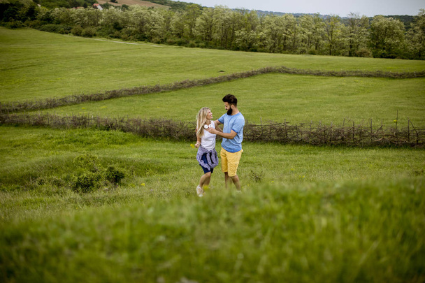 Amar a la joven pareja disfrutando de un paseo por la tierra de hierba en un día de verano
 - Foto, imagen