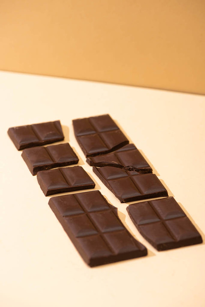γλυκιά νόστιμη σπασμένη μαύρη σοκολάτα σε μπεζ φόντο - Φωτογραφία, εικόνα
