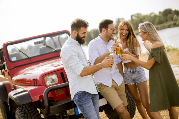 Groep jonge mensen drinken en plezier maken met de auto buiten op een zonnige warme zomerdag - Foto, afbeelding