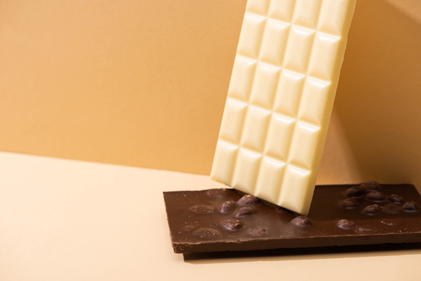 Bej arka planda fındıklı lezzetli beyaz ve siyah çikolatalar. - Fotoğraf, Görsel