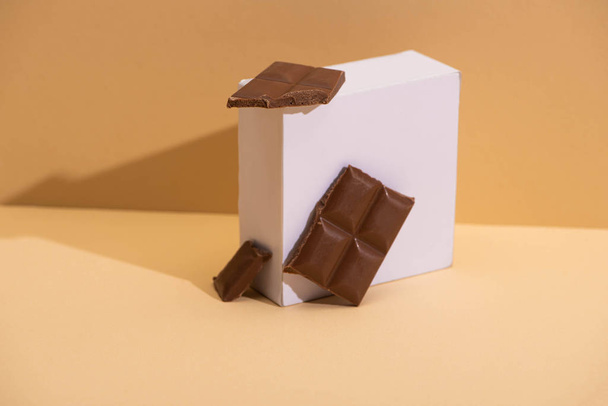 pyszne kawałki czekolady mlecznej i kwadratowy sześcian na beżowym tle - Zdjęcie, obraz