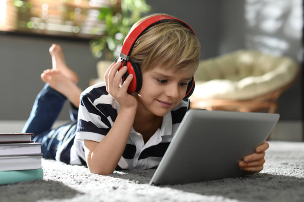 Cute little boy with headphones and tablet listening to audiobook at home - Photo, Image