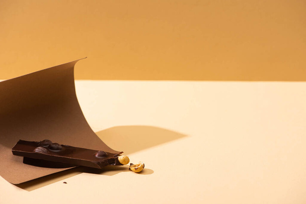 delicioso chocolate negro con nueces pieza, papel sobre fondo beige
 - Foto, Imagen