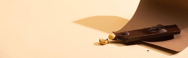 delicious dark chocolate with nuts piece, paper on beige background, panoramic shot - Valokuva, kuva